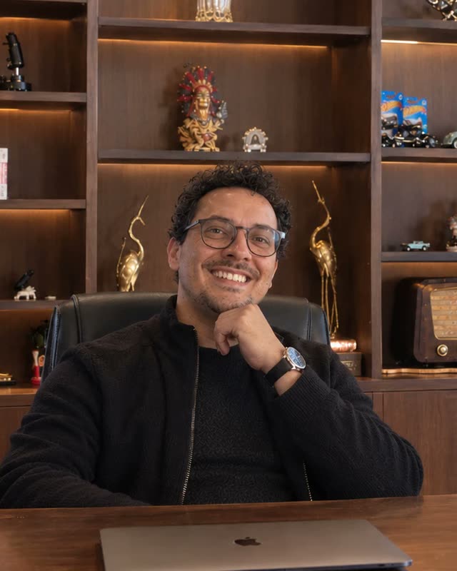 Wagner Borges de Lima sorrindo, sentado à mesa do escritório, com uma estante de madeira iluminada ao fundo.